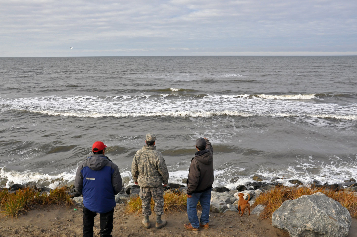 three men looking out over gray ocean water