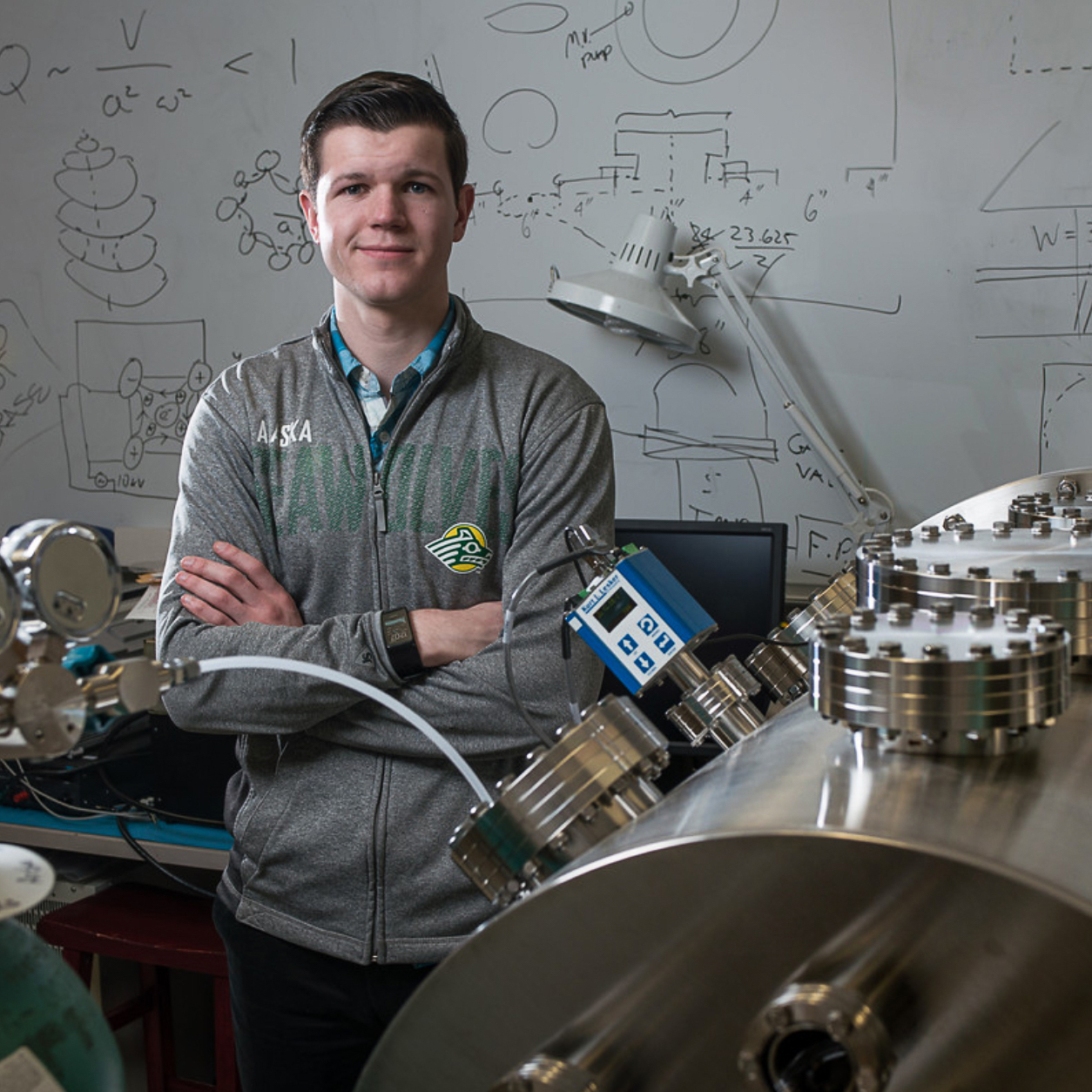 
Student smiling while standing beside a vacuum chamber with digital pressure gauge in a laboratory
