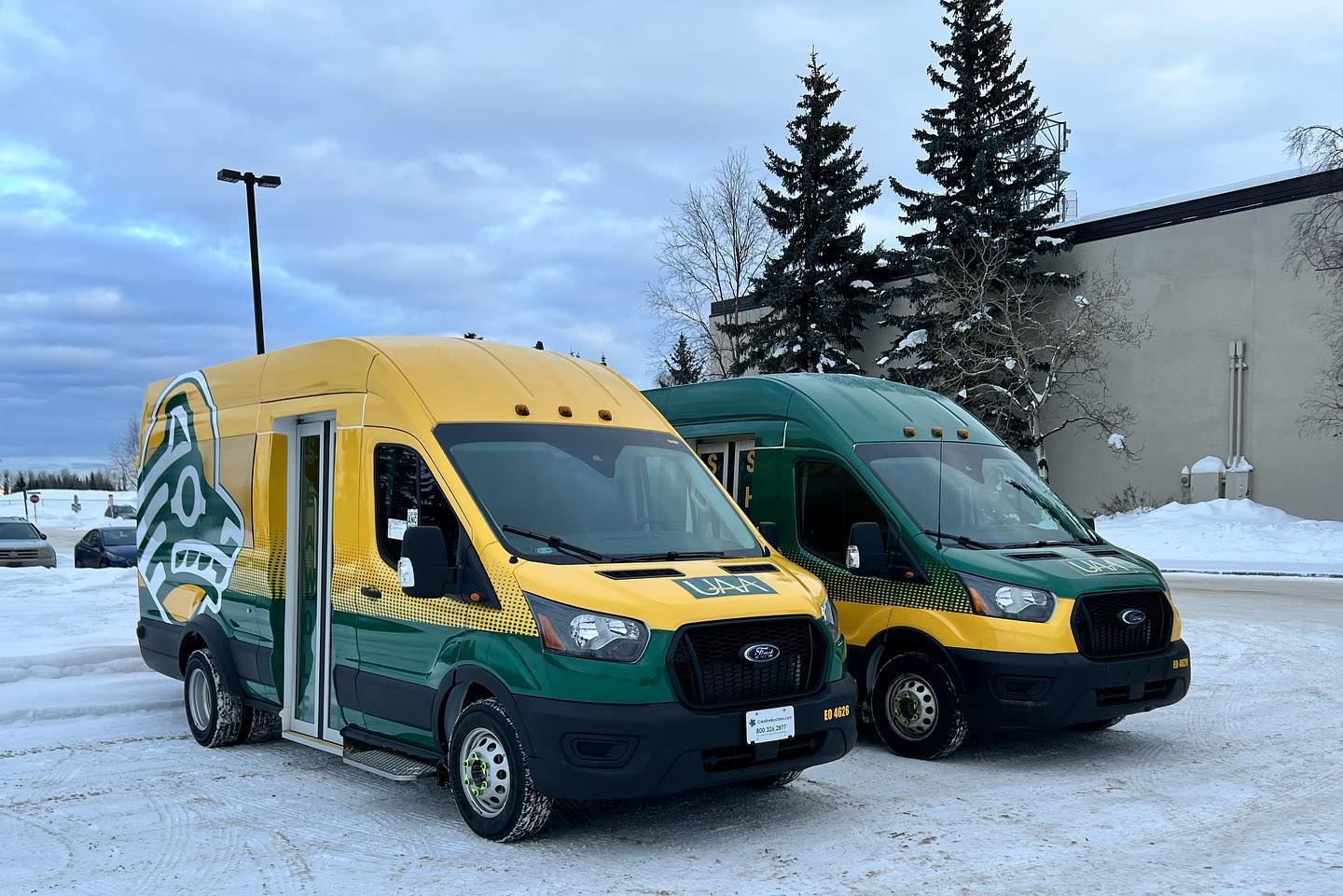 The 2 Seawolf shuttles sitting in the campus parking lot on a snowy day.