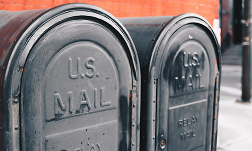 Two black roadside mailboxes in front of a brick building