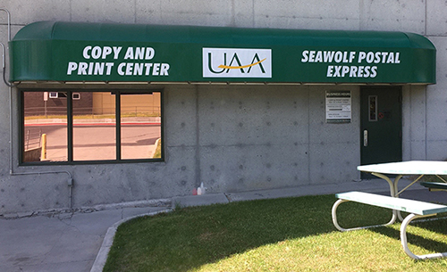 Entrance with green awning that says "Copy and Print Center" and "Seawolf Postal Express" in the summer.