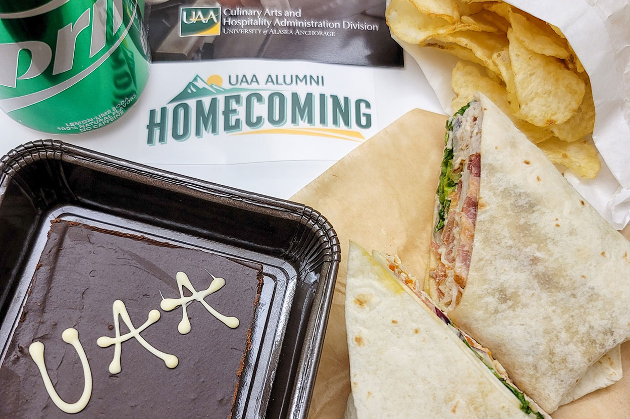 UAA Alumni Homecoming logo with turkey wrap, chips, brownie and Sprite