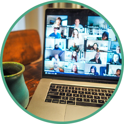 Open laptop sitting on wooden desktop with green mug and with Zoom conference showing on screen