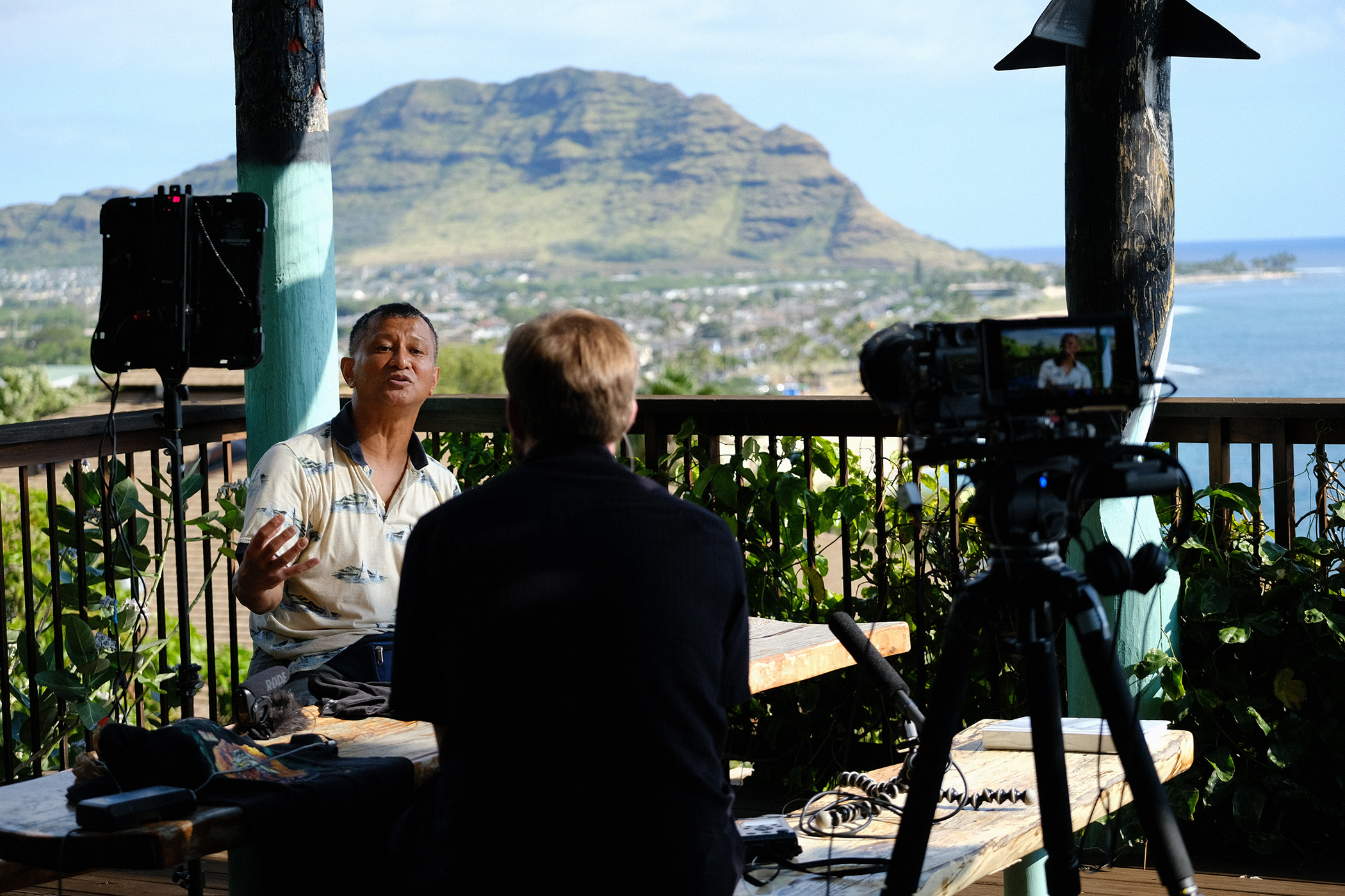 man on patio answering questions with a camera in foreground and hawaiian mountain in background