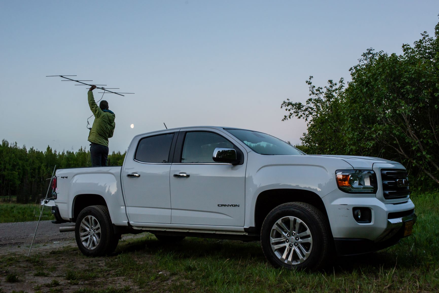 A researcher holds an antenna aloft while standing in the bed of a white truck at dusk
