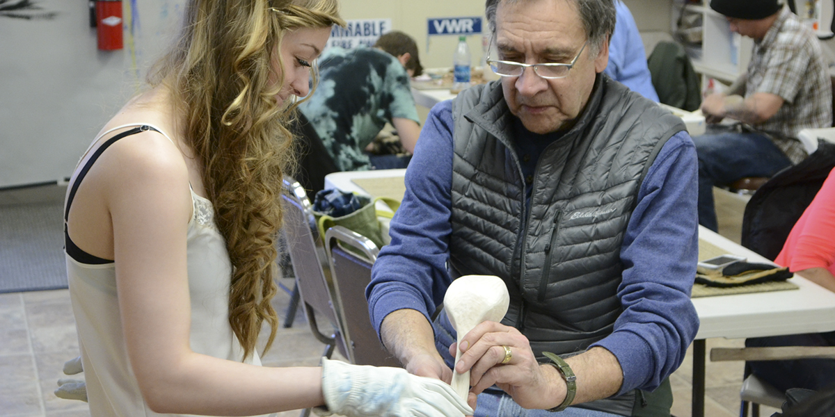 Instructor Alvin Amason examining student's carving