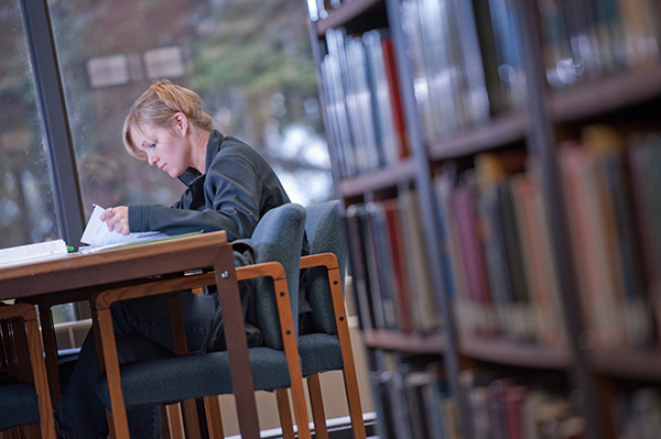 Student seated at a desk in a library, looking over some papers