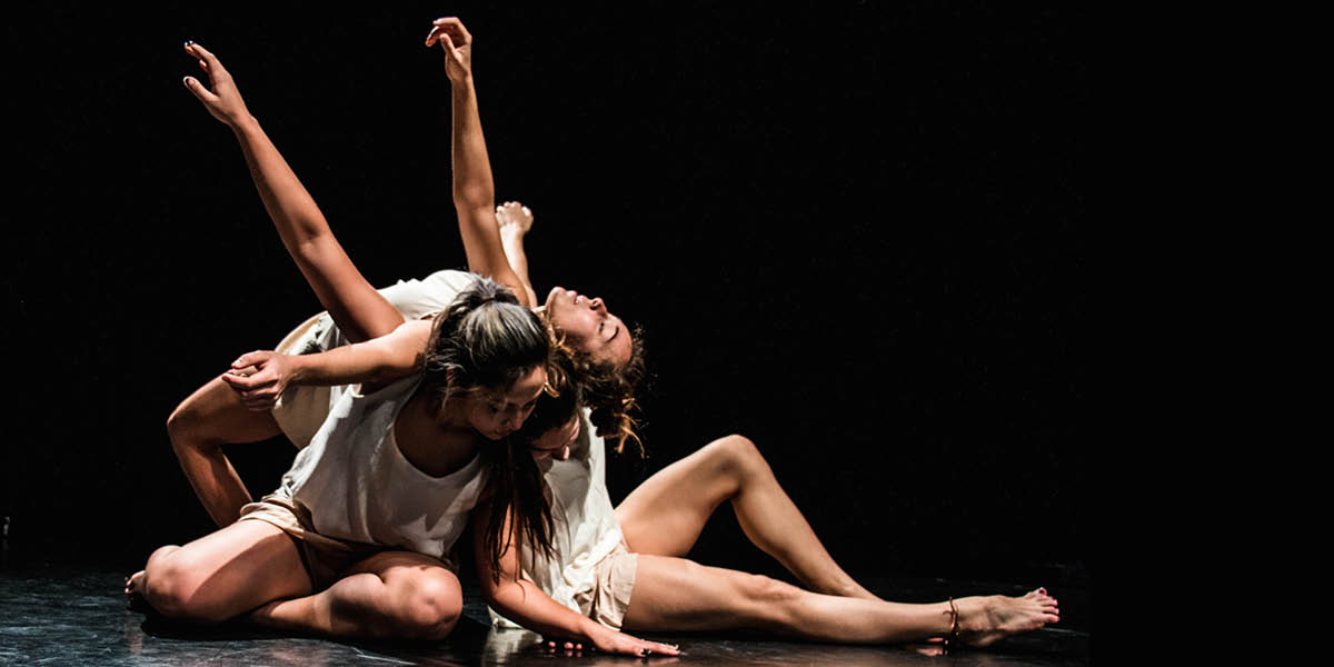 one dancer draped over the back of two dancers sitting on the floor