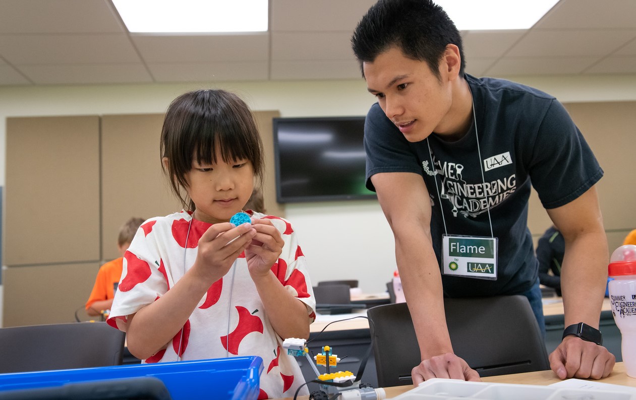 A student employee assisting a summer camp participant in building a robot.