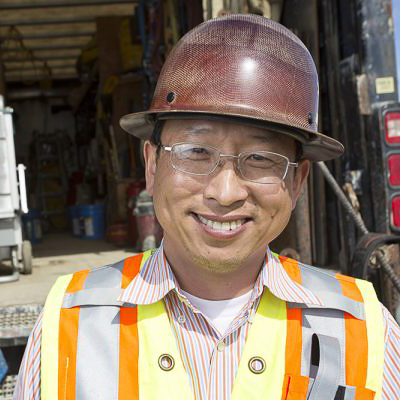 Headshot of alumni Chong Kim wearing a hardhat and safety vest at a jobsite in south anchorage.