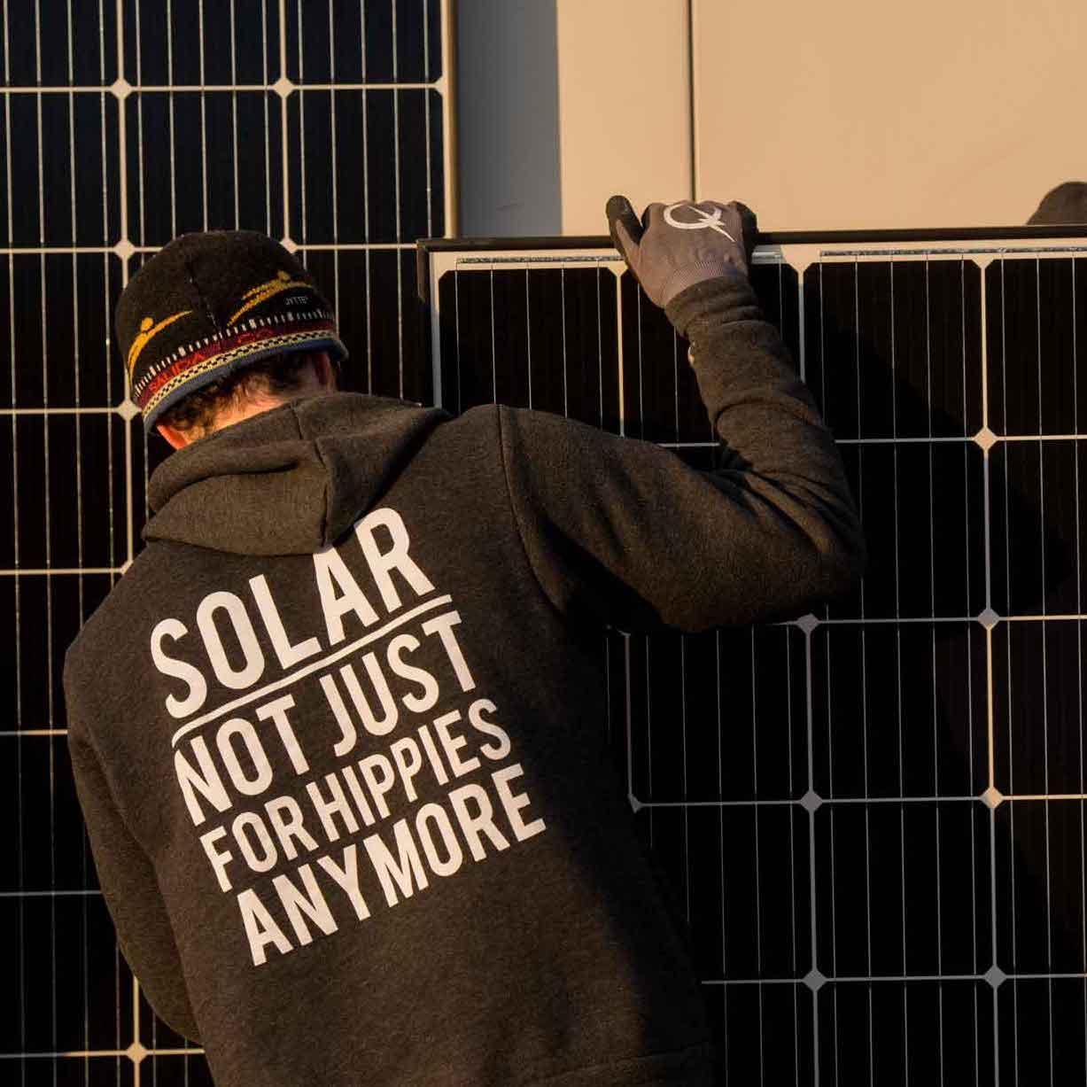man installing solar panel with a hoodie that says "Solar, not just for hippies anymore" printed on the back.
