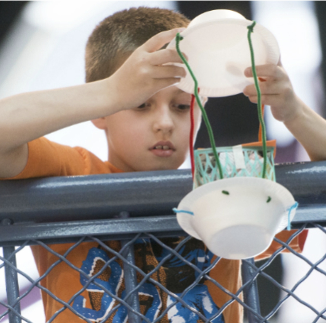 A child holds an egg drop contraption over a railing
