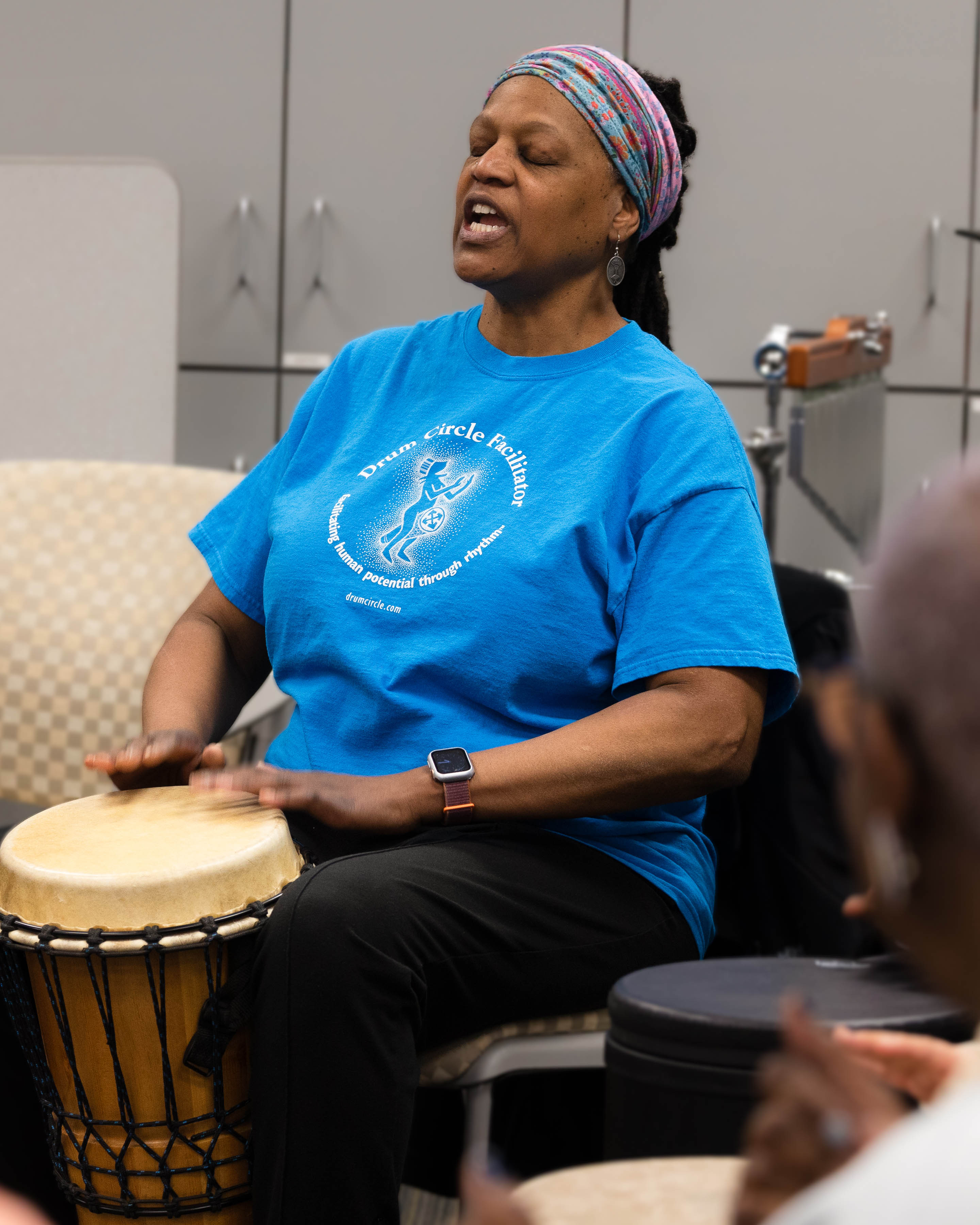 gail jackson singing in chair and playing drum
