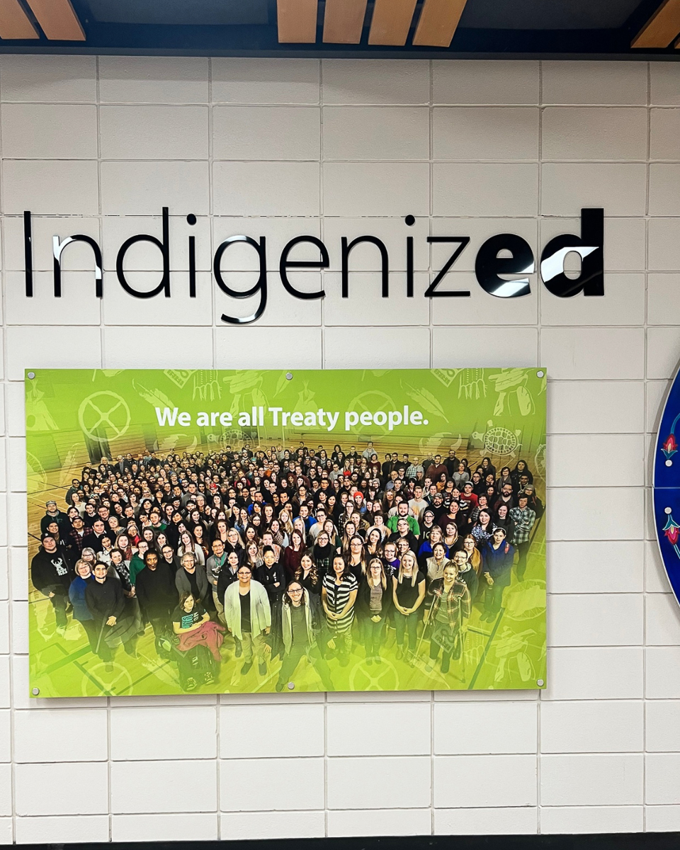 sign on white wall with large group of people reading "indigenized, we are all treaty people"