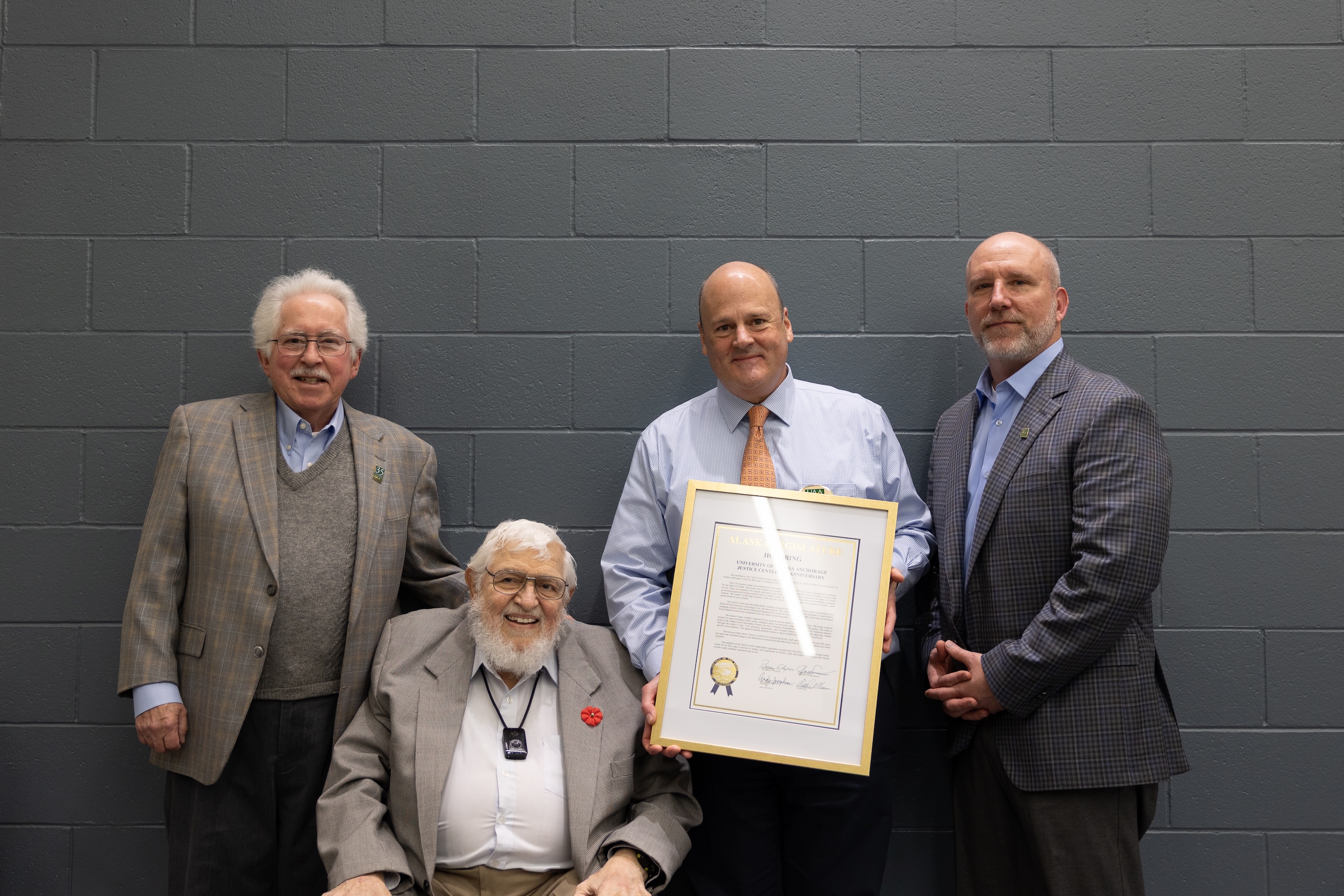 Professors Emeriti Allan Barnes and John Angell are next to Associate Dean Andre Rosay and Assistant Dean Brad Myrstol. Rosay is holding the framed legislative citation. All are smiling