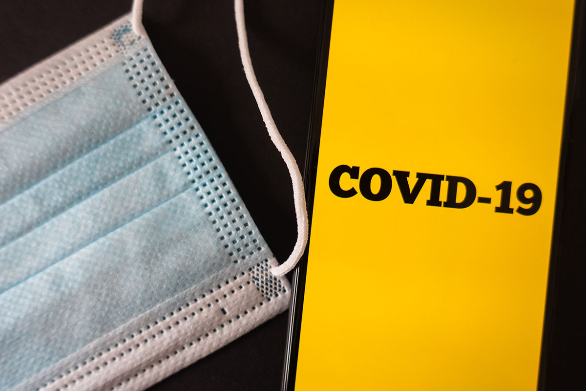 A face mask next to a phone that says COVID-19 on its screen