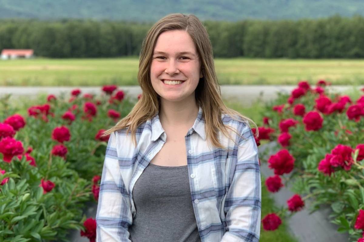 Keely Livingston, MPH student, smiles as she stands in a field of red flowers wearing a flannel shirt. 