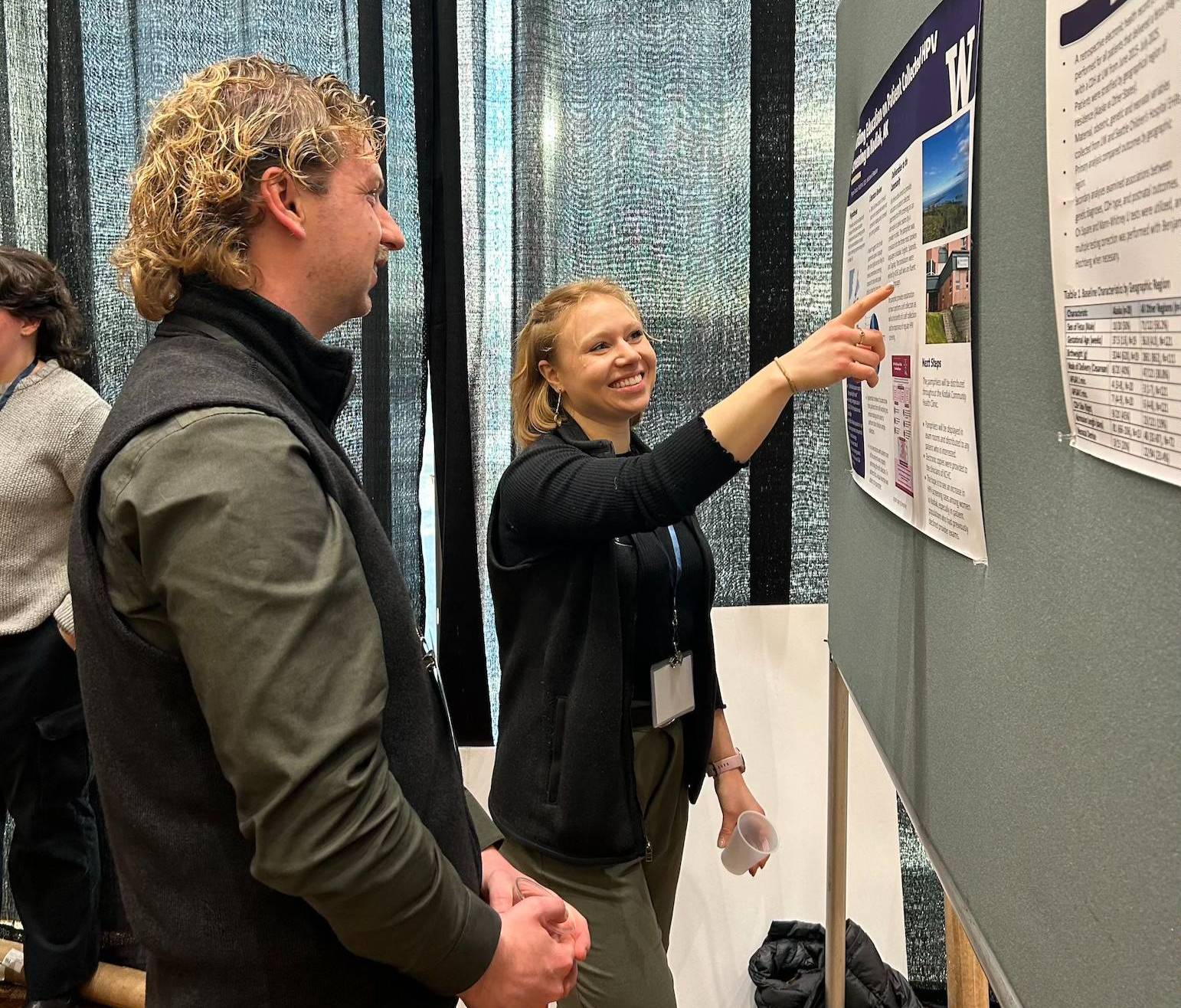 A WWAMI student stands in front of her poster and points to an image for another student, who stands next to her. 