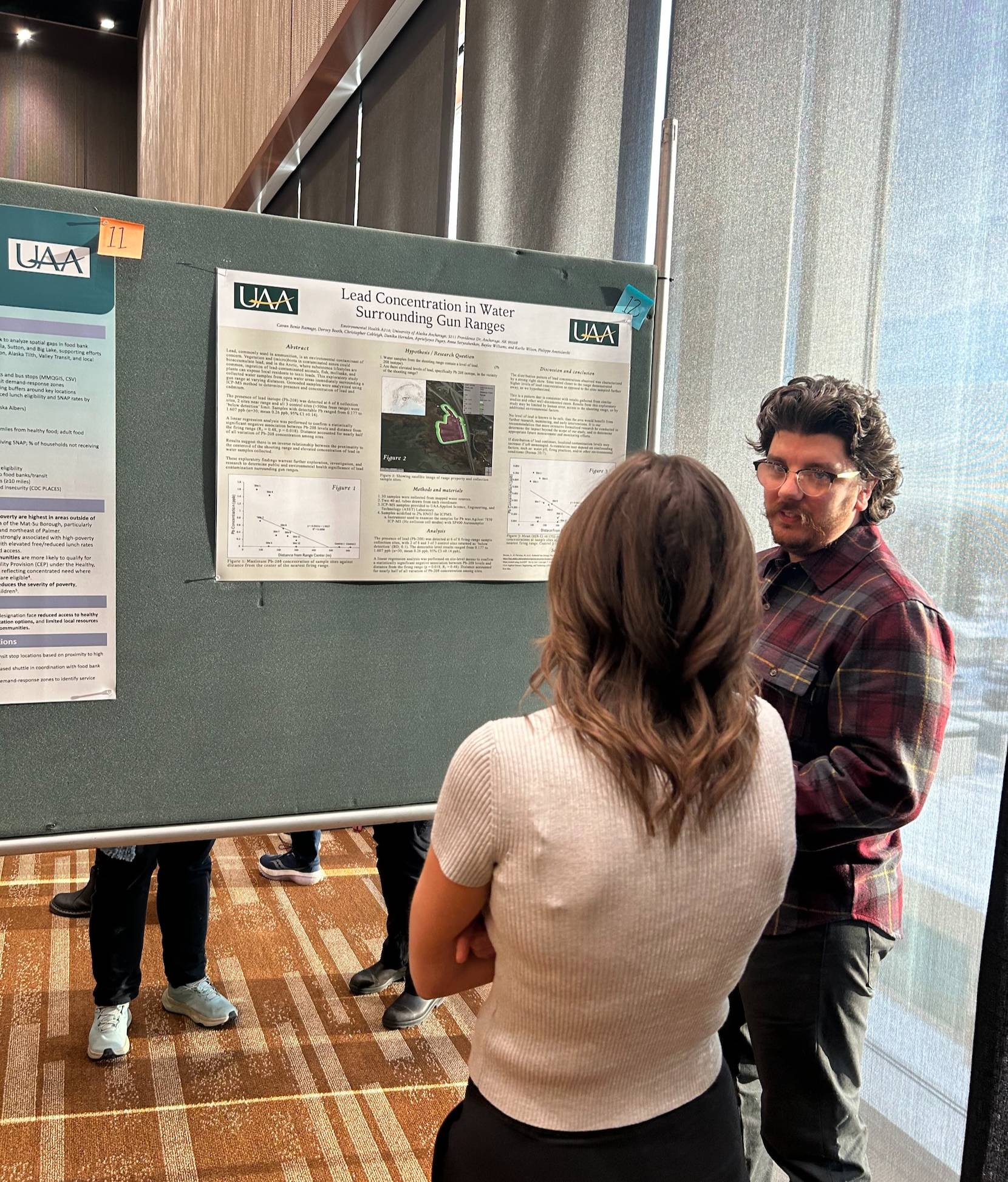 A student stands in front of his poster, titled "Lead Concentration in Water Surrounding Gun Ranges." He is speaking to a conference attendee standing in front of him. 