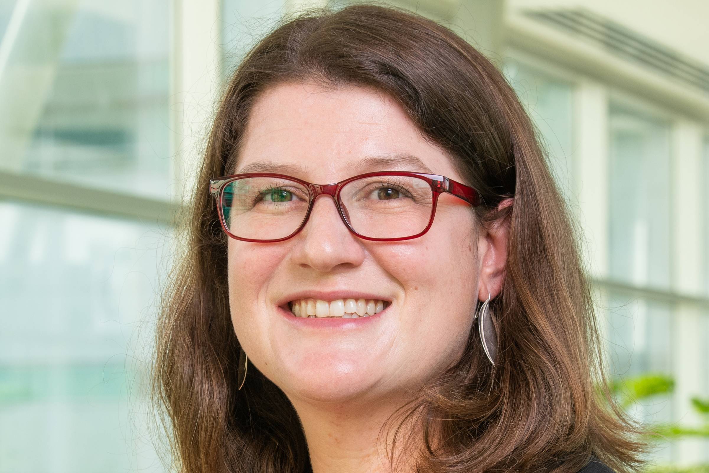 Dr. Corrie Whitmore stands in front of windows on the UAA campus. She is wearing glasses and smiling. 
