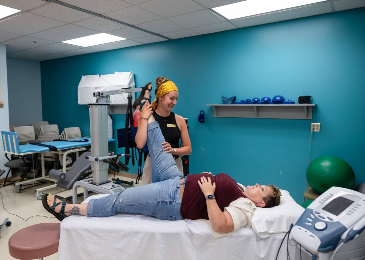 A UAA faculty member guiding a patient lifting weights over their head while laying down.