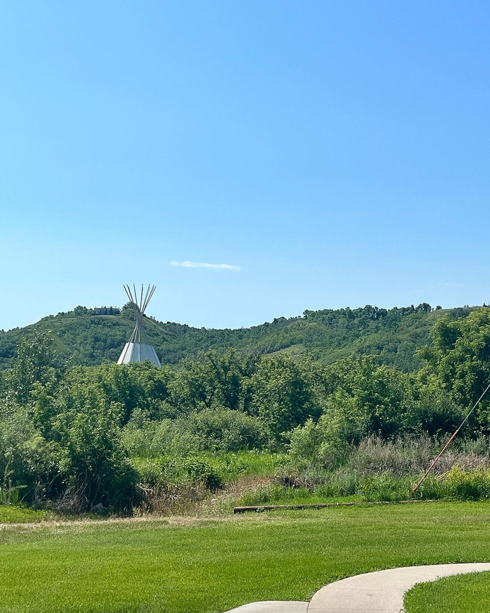 wooded area in daytime with paved walkway and teepee in distance