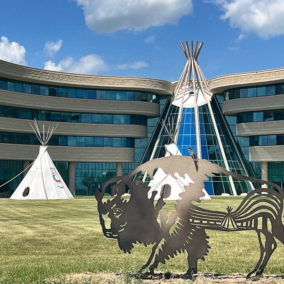metal buffalo sculpture in front of building shaped like teepee and regular teepee