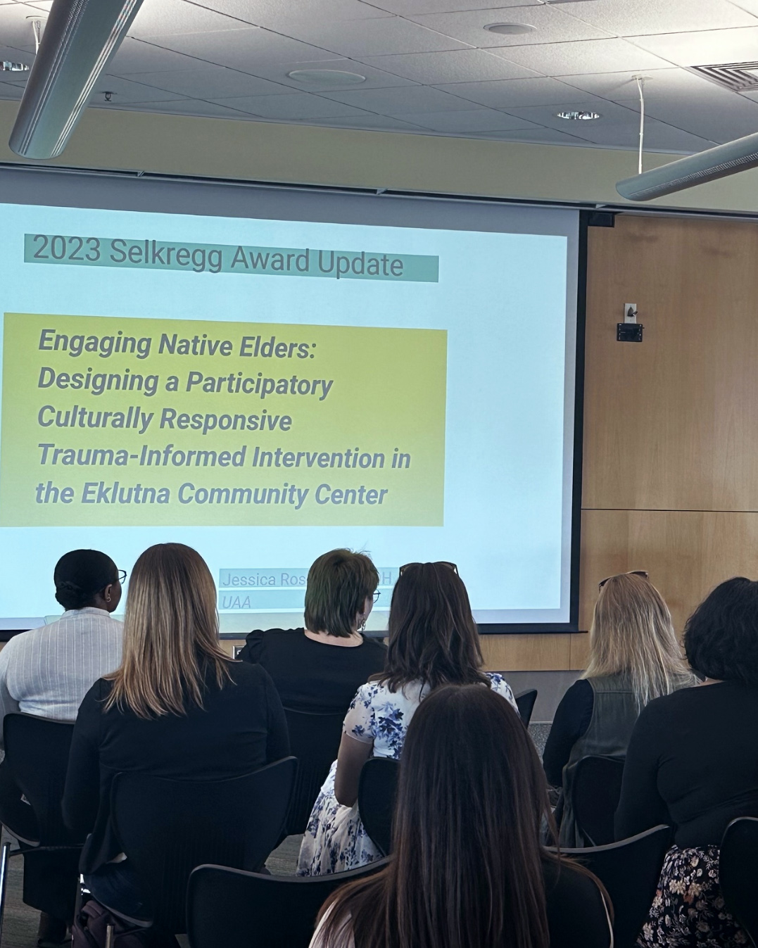 group of people staring at projector screen and sitting chairs in room