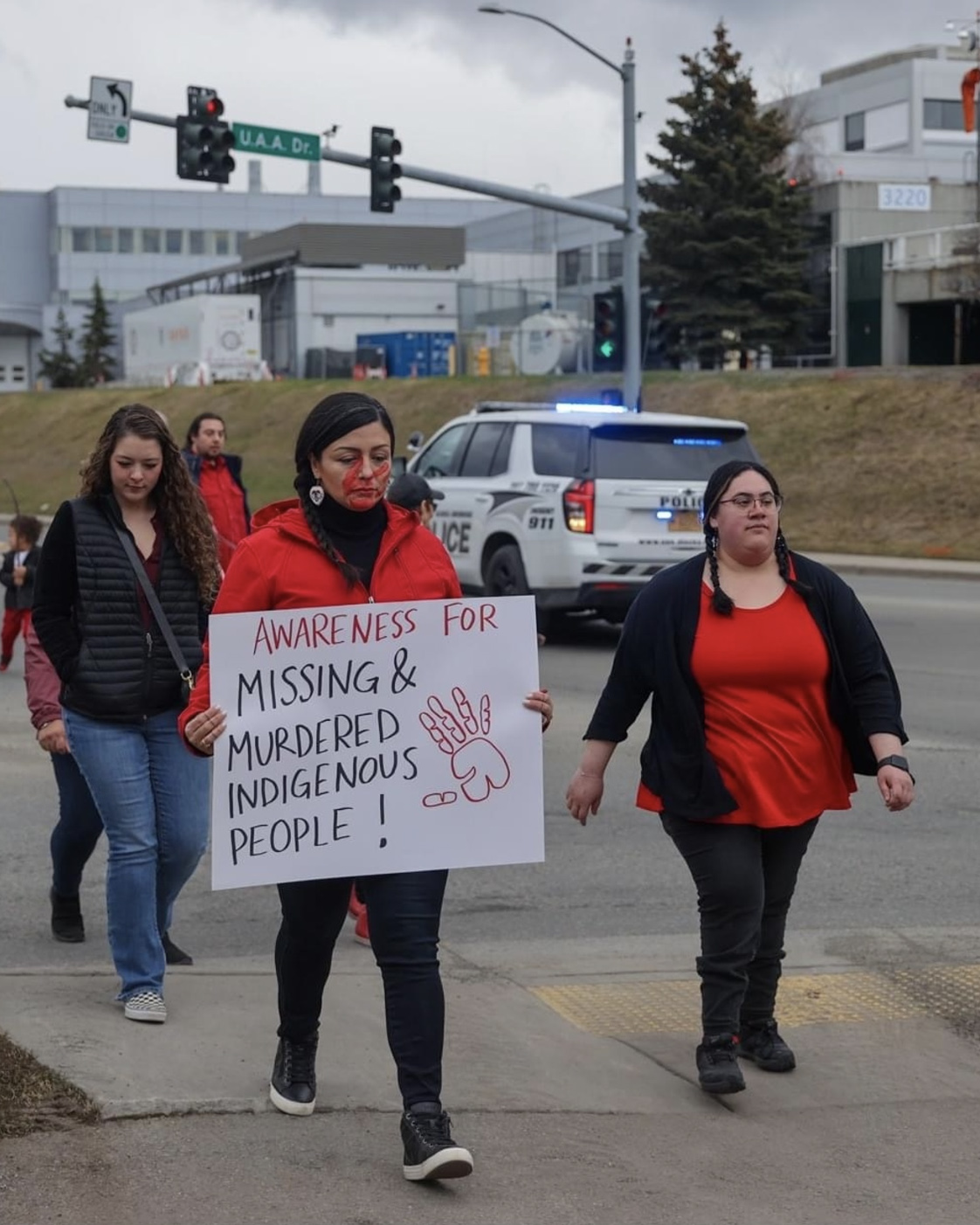 jessica ross walking with group of people on sidewalk carrying sign that reads "awearness for missing and murdered Indigenous people