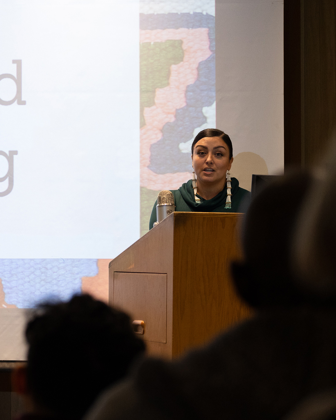 jessica ross speaking to crowd at podium infront of projector screen
