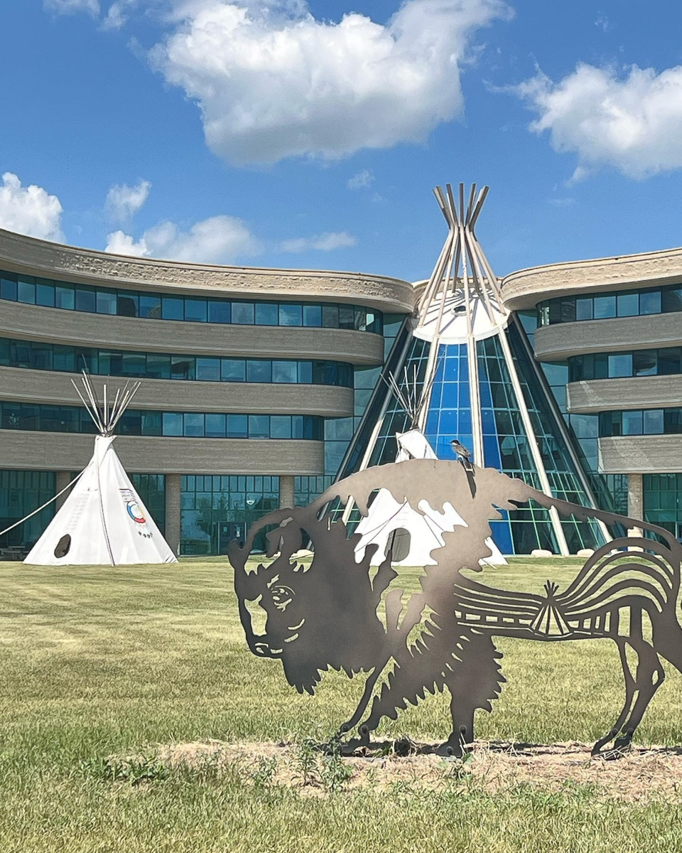 metal buffalo sculpture in front of building shaped like teepee and regular teepee