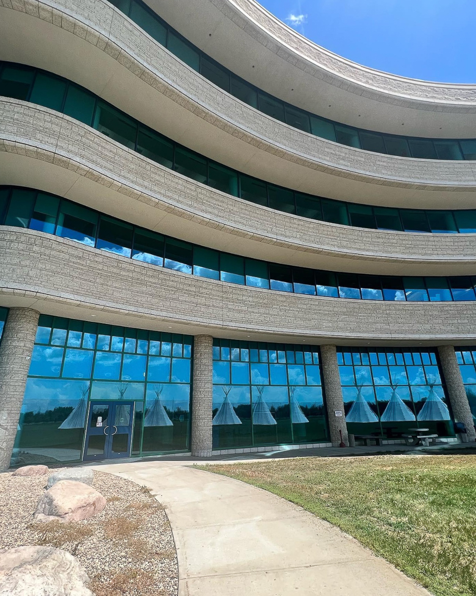 curved builsing with wall of windos reflecting teepees in feild