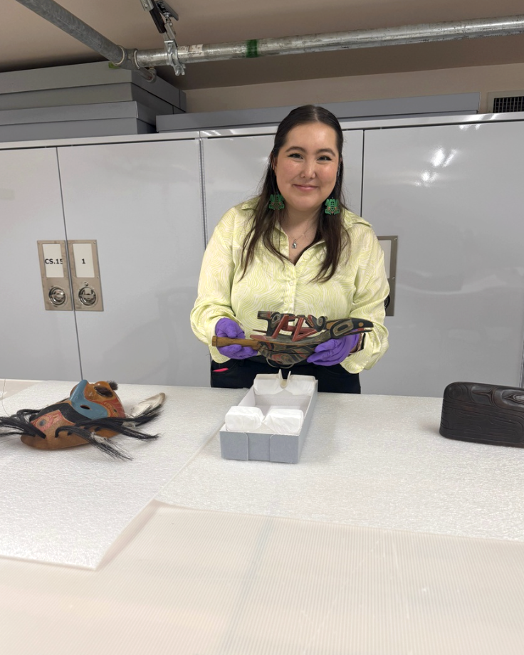 Jelly Firmin smiling and holding wooden mask on Styrofoam covered table 