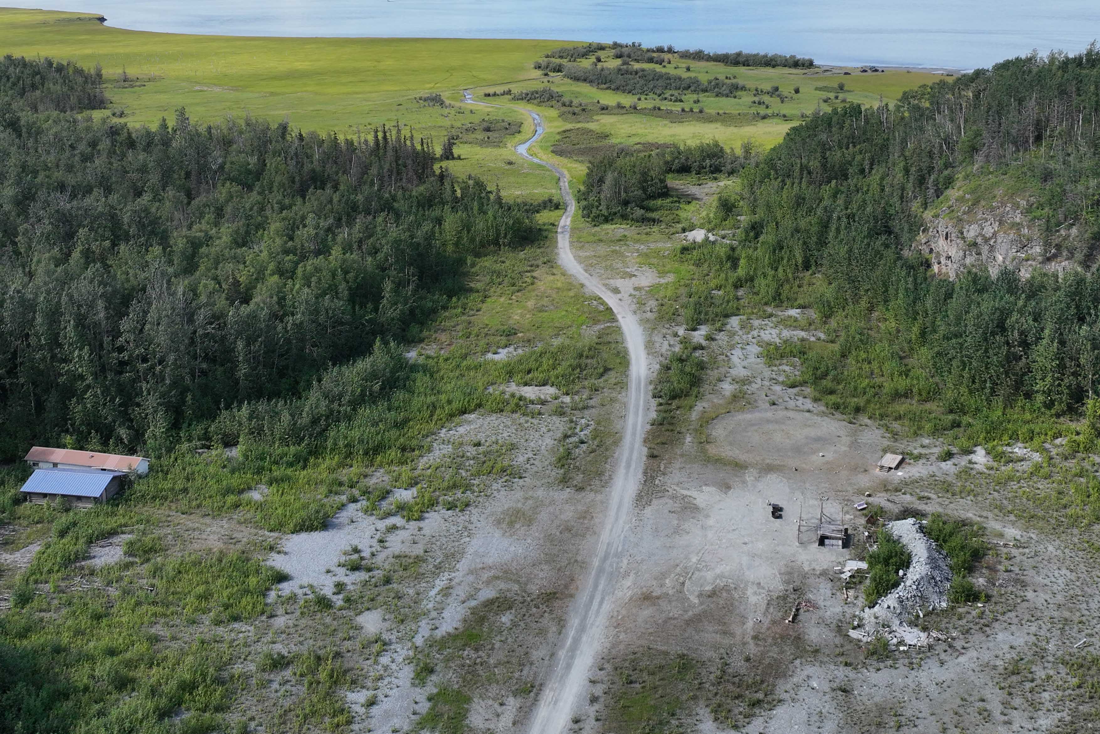 birds eye view of heavily forsested land, river, green feild and 2 small buildigs