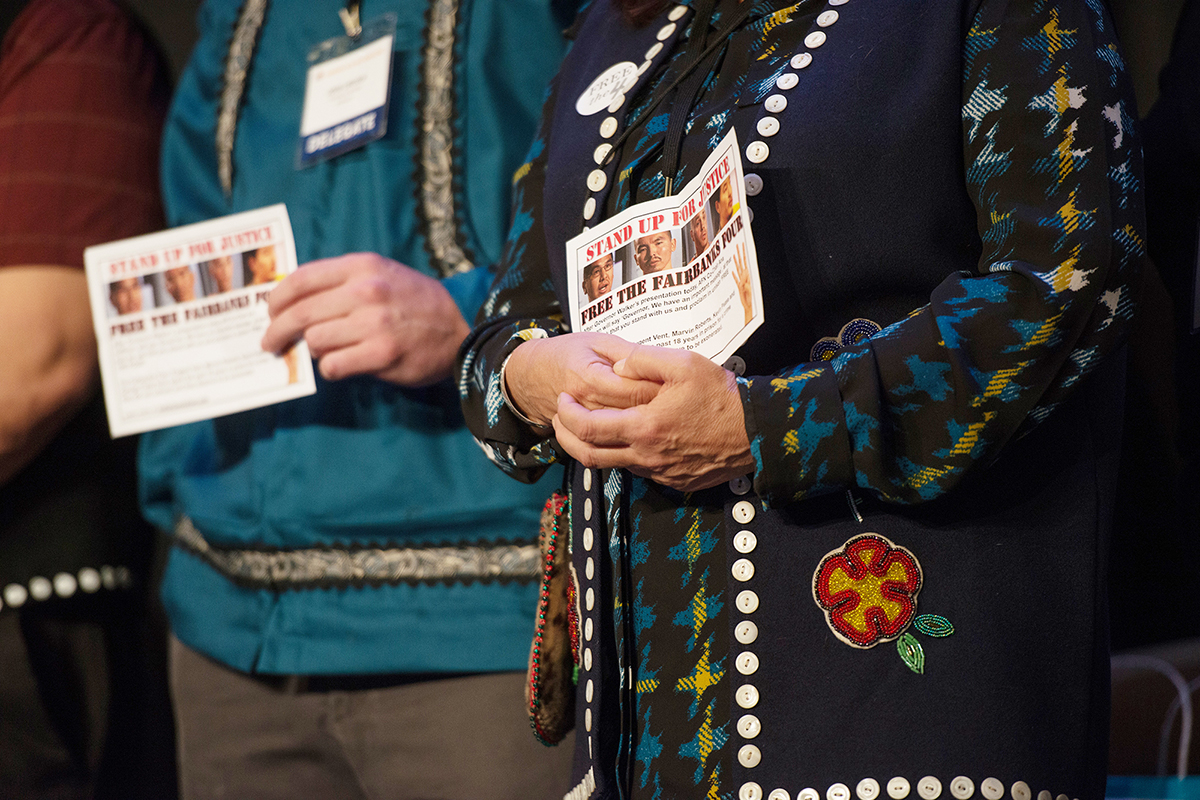 People holding a flyer that has the Fairbanks Four featured
