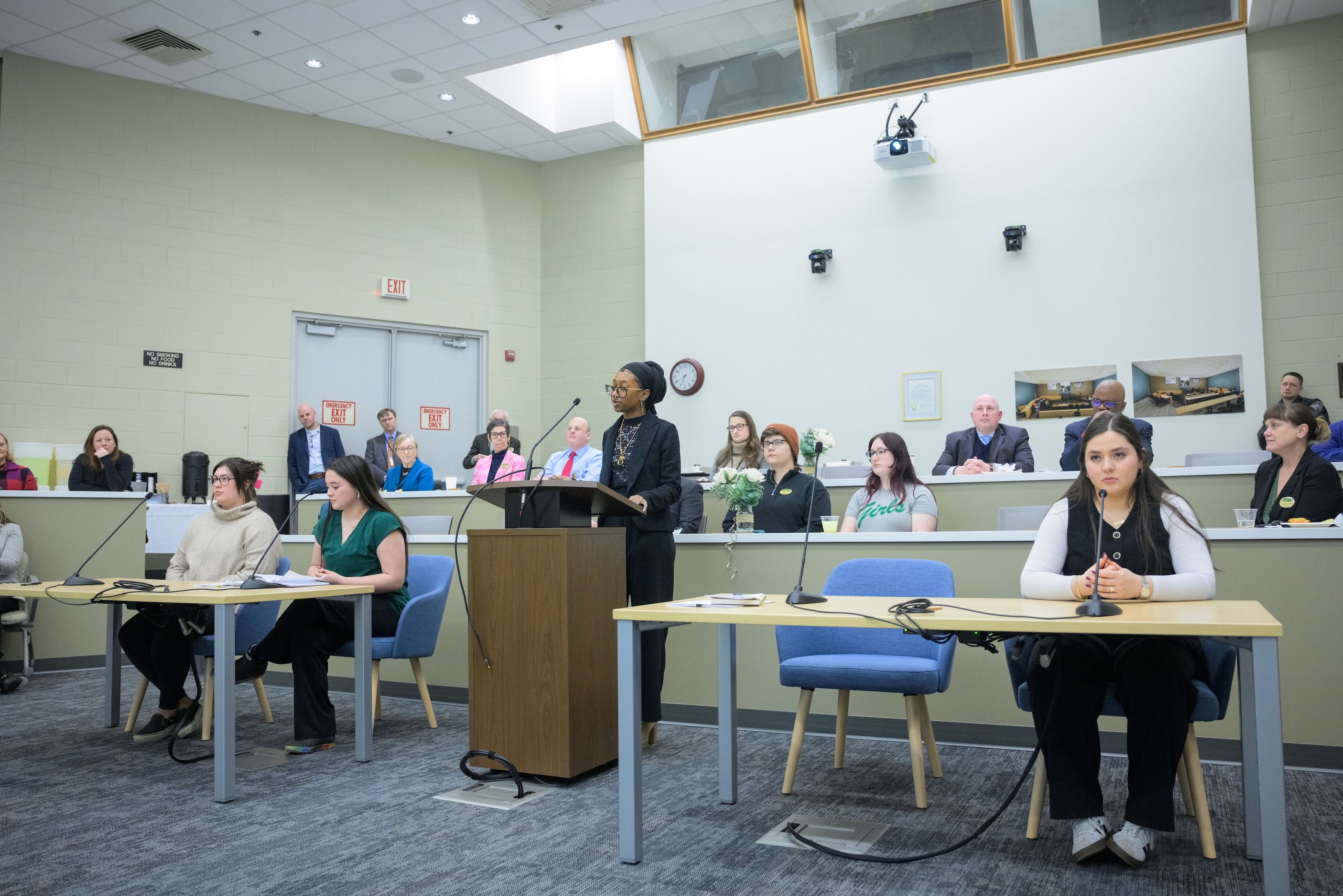 Students engage in a trial simulation in the new Havelock Classroom. One student stands at the podium and speaks into the microphone. On either side, students sit at the prosecution and defense tables. Audience members observe from the gallery area behind them.