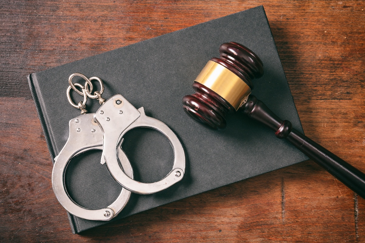 Handcuffs and a gavel on a book on a wooden desk