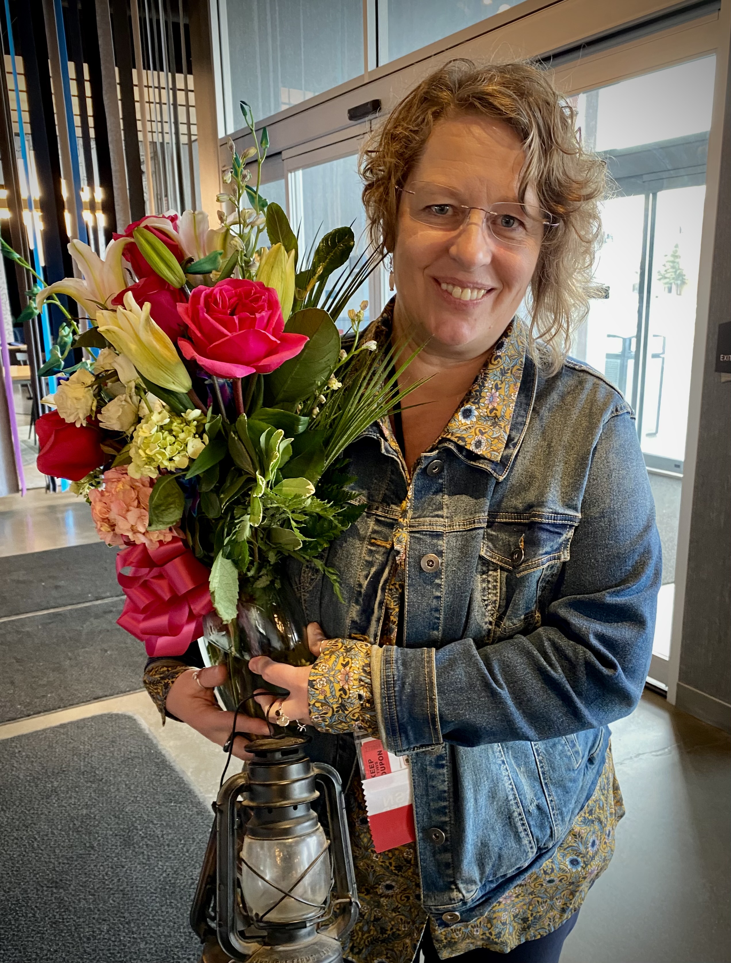 Wendy DeGraffenried holds a bouquet of flowers in a vase and a lanter after receiving the 2023 National School Nurse of the Year Award. She is smiling at the camera.