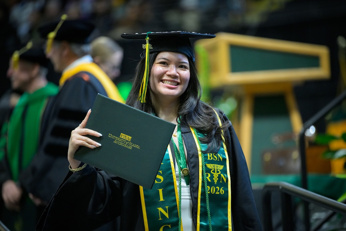 School of Nursing graduate smiling holding their degree