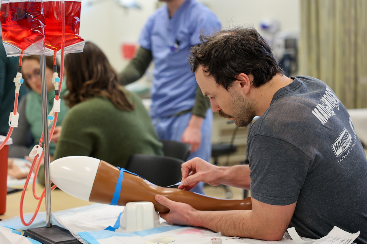 a student practices starting an IV on a trainer arm