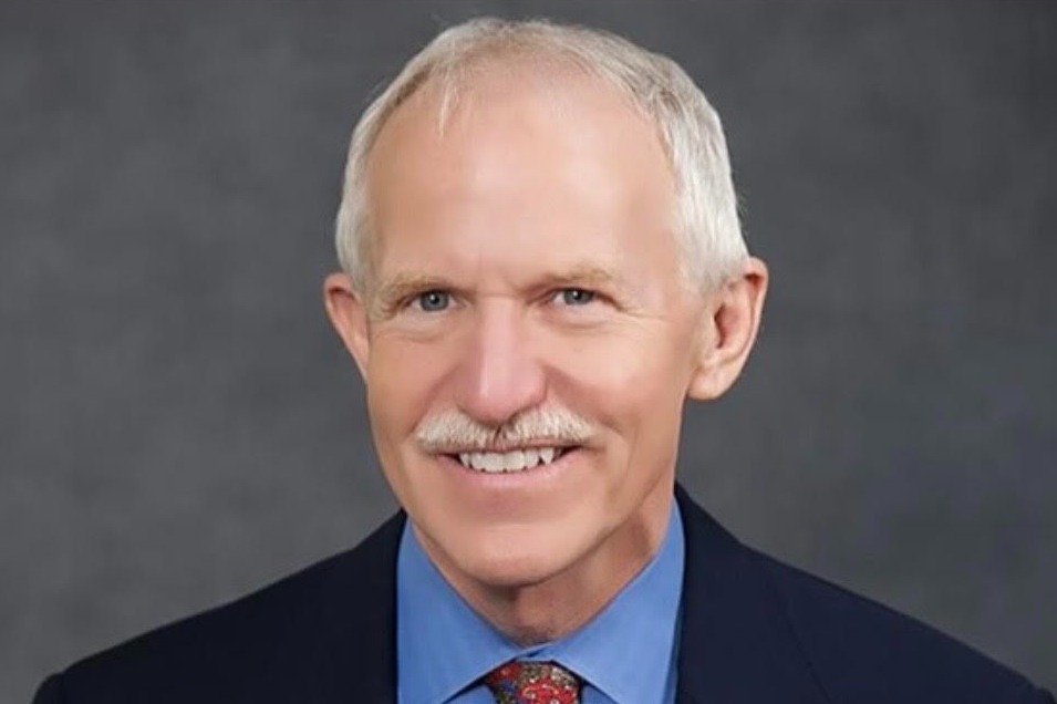 Dr. Jay Butler wears a suit and smiles at the camera against a dark gray backdrop.