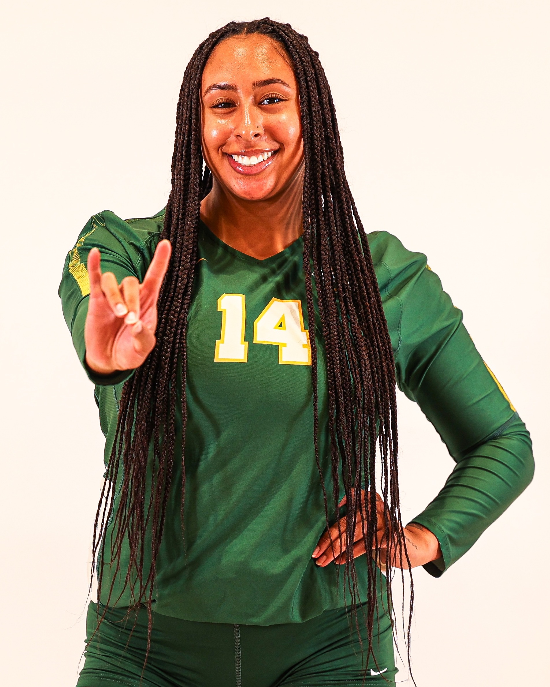 Bella Byrne is wearing a green long-sleeved jersey. One hand is raised, with the pointer and pinky finger extended.