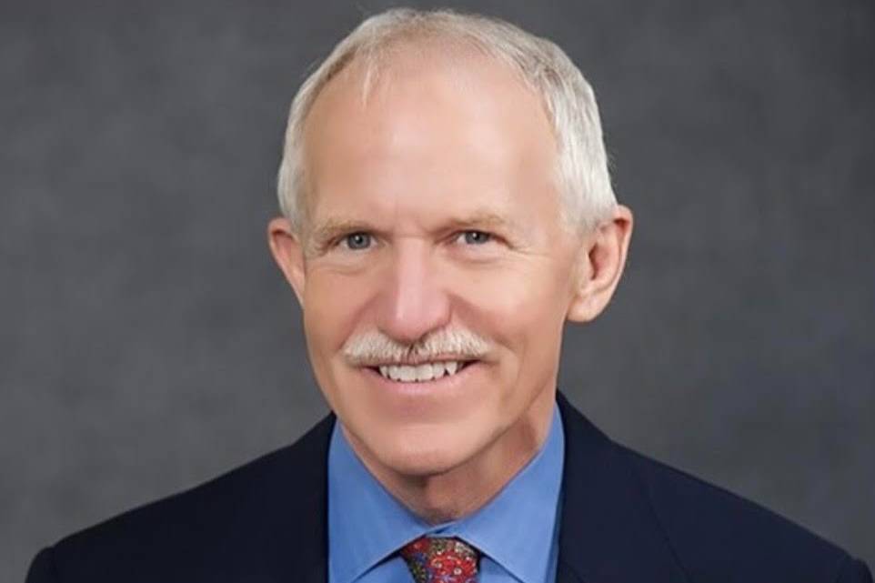 Dr. Jay Butler wears a suit and smiles at the camera against a dark gray backdrop.