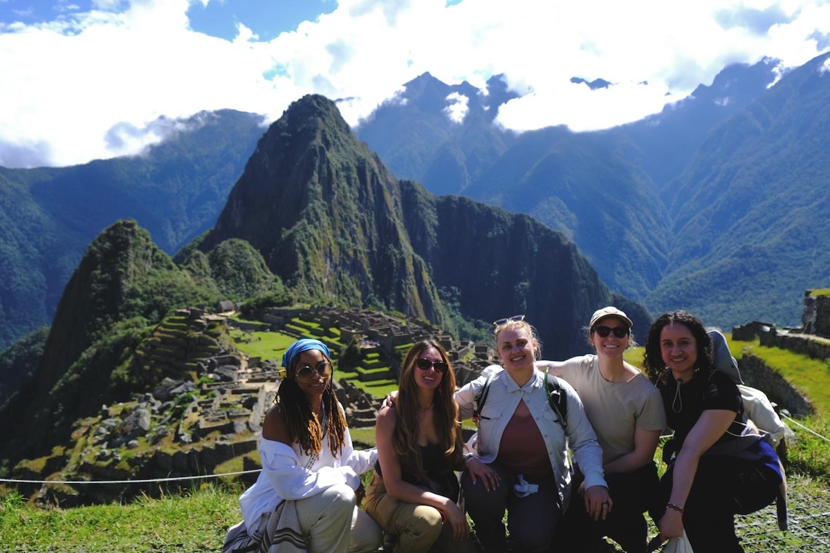 Five people pose in front of a historical site and mountainous background