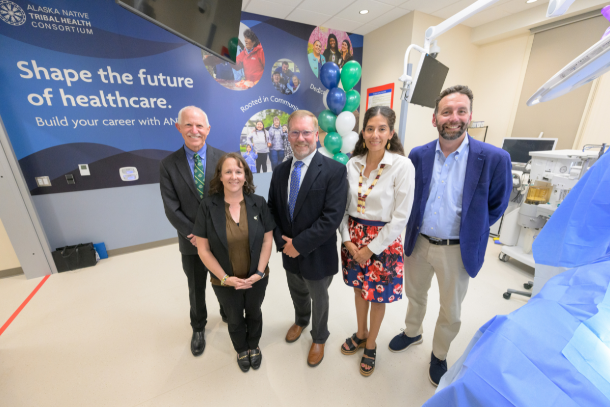Three men and two women smiling for a photo in a medical simulation laboratory