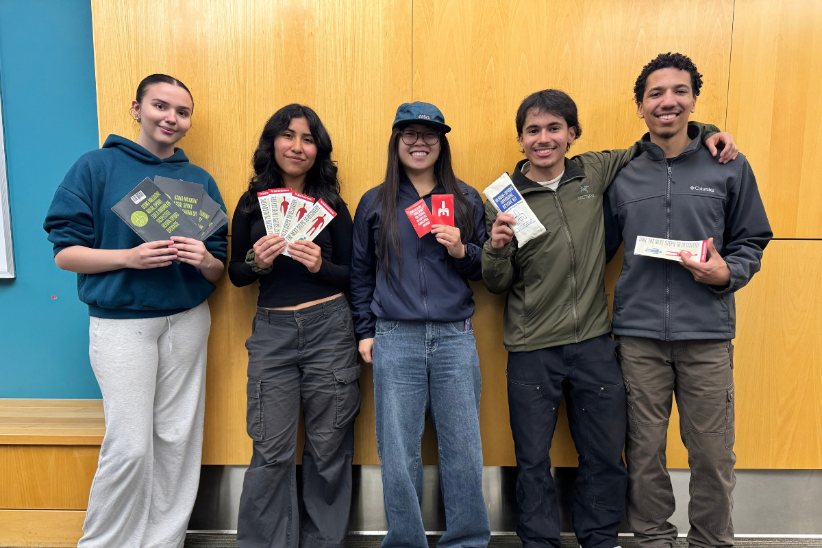 Five people standing in front of a wooden wall holding up brochures and other medical supplies