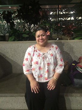 Photo of Carolyn Fautanu sitting on a bench with a flower behind her left ear