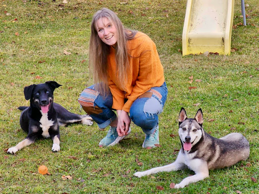 Marsha Olson squatting down between two dogs