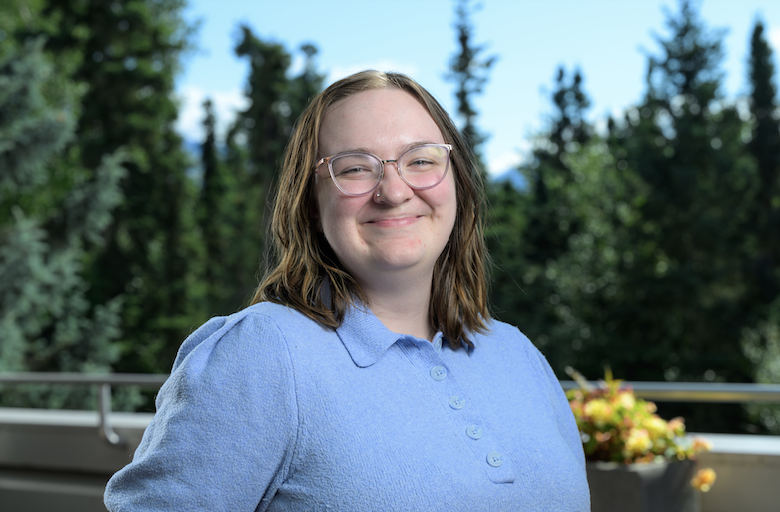 Rachel Nill smiling and posing in front of trees on the UAA campus