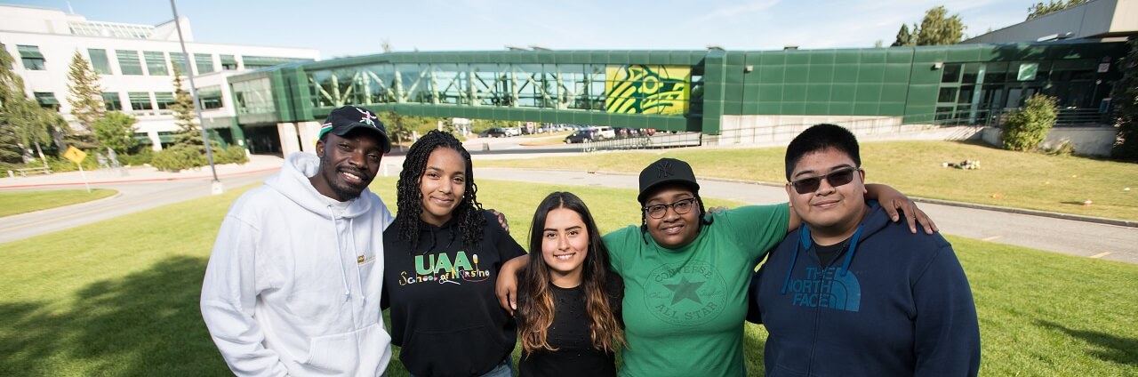 A group of UAA orientation leaders take a photo in front of the campus skybridge.